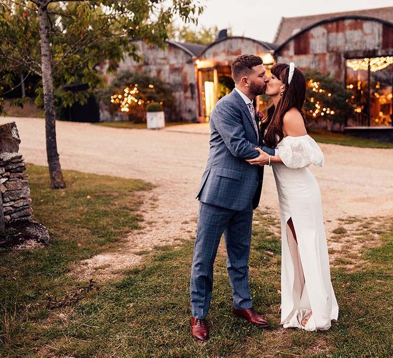 Bride & groom kiss in front of the Stone Barn Cotswolds on their wedding day