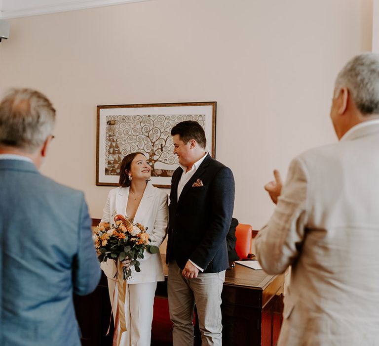 Islington Town Hall wedding ceremony with bride in white jacket holding an orange flower bouquet 