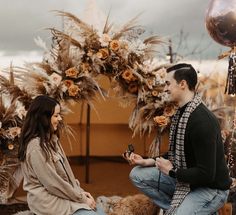 Wedding proposal with groom-to-be down on one knee popping he question to his girlfriend