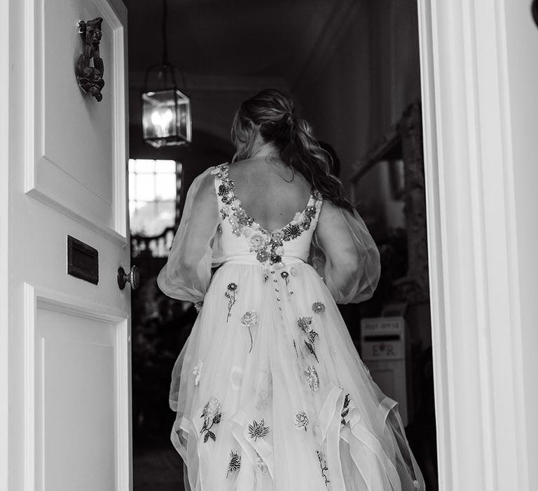 Bride with ponytail and low back wedding dress with tulle train and floral embroidery walks through door at Iscoyd Park