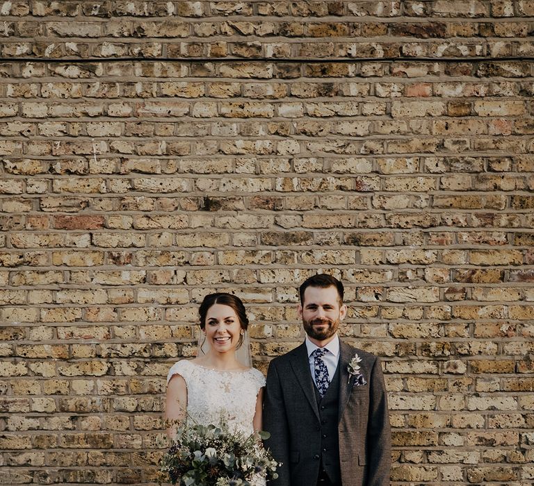 Bride & groom stand in front of brick wall on their wedding day