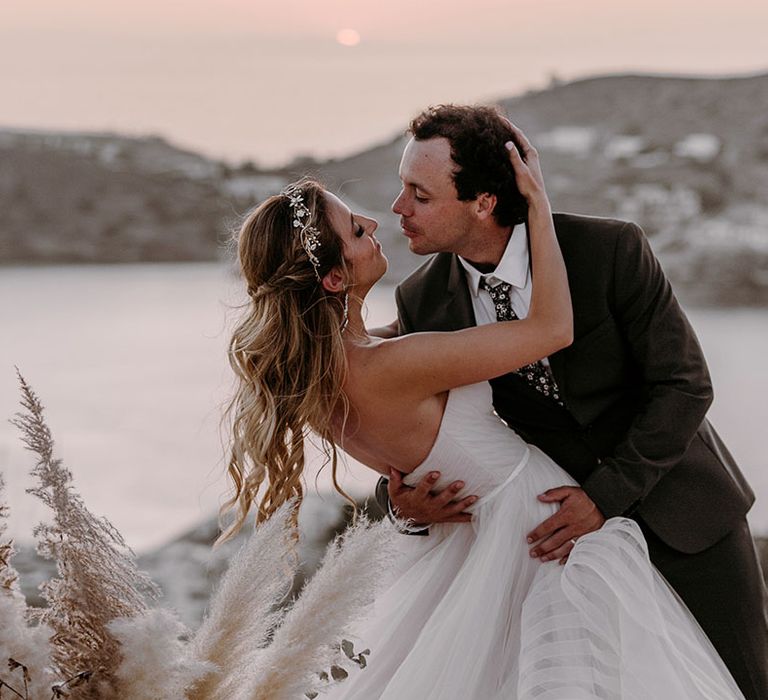 Groom leans his bride back on her wedding day to kiss outdoors 