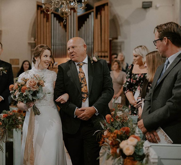 Bride walks down the aisle lined with orange flowers clutching bouquet