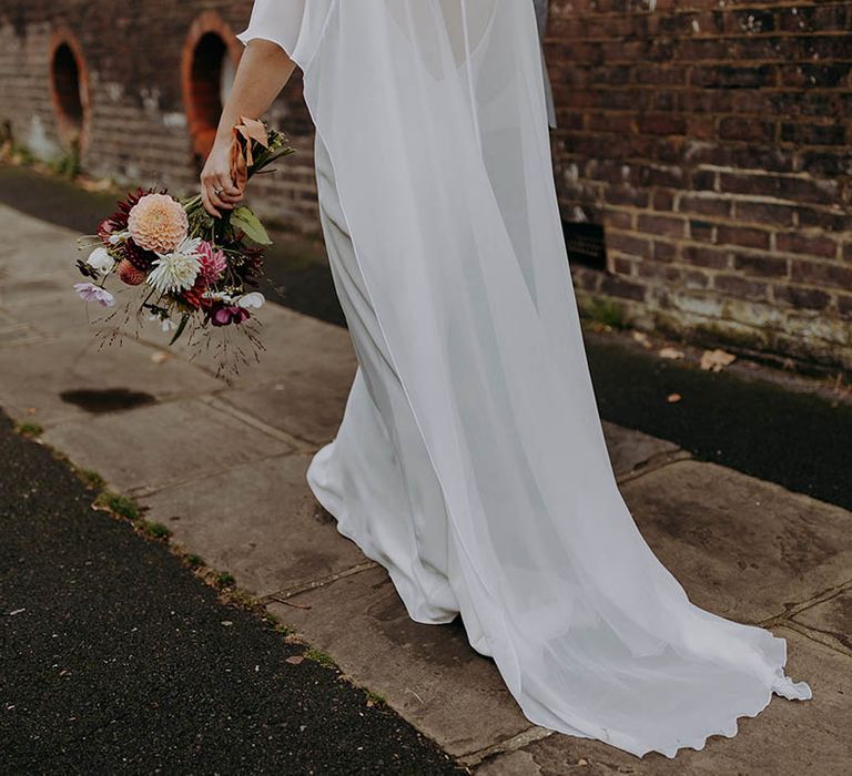 Bride walks down the road wearing sample wedding dress with cape 