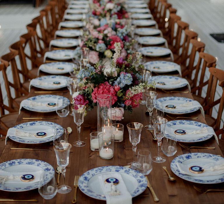 Long banquet wooden table complete with bright florals, white and blue china plates and hanging chandeliers 