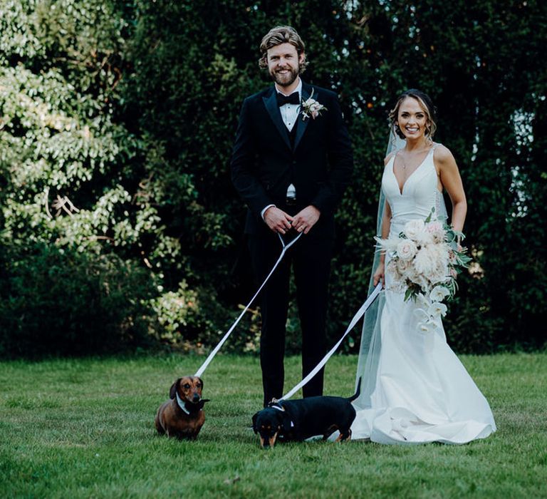 Groom in black tuxedo and bride in mermaid fishtail wedding dress with two dachshund in dog wedding outfits at Elmore Court