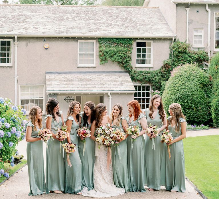 Bride in strapless lace wedding dress with her bridesmaids in sage green v-neck dresses and wildflower bouquets 