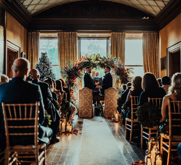 Christmas winter wedding at castle Leslie estate with Christmas tree as grooms get married in front of floral moongate and damask chairs