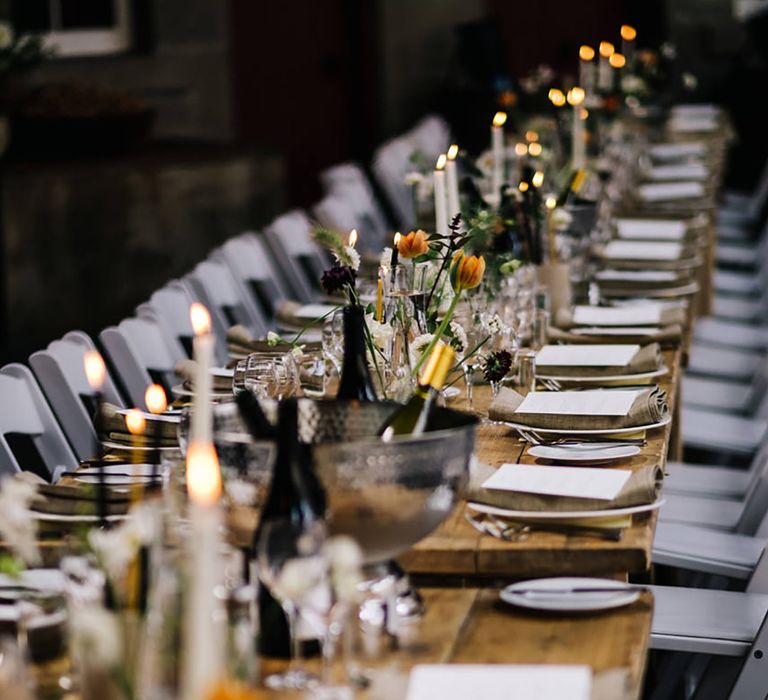 Tablescape with orange, yellow and dark flower arrangements with white candles and ice buckets of wine