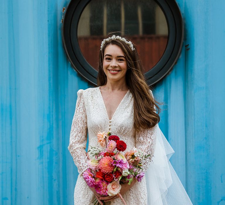 Bride in lace buttoned Rixo wedding dress and pearl cluster headband with long brown hair holding pink and red wedding bouquet 