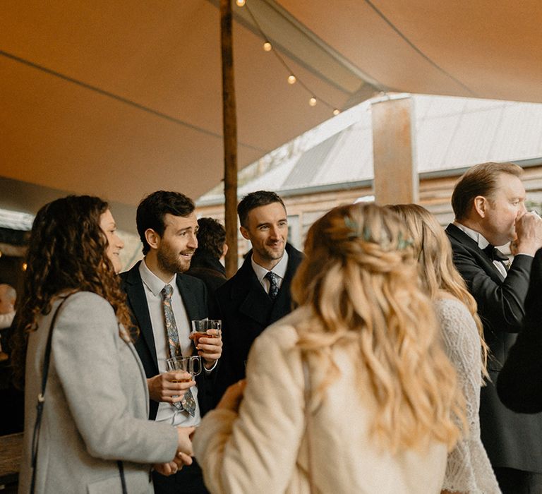 Wedding guests socialise under canopy for outdoor drinks reception