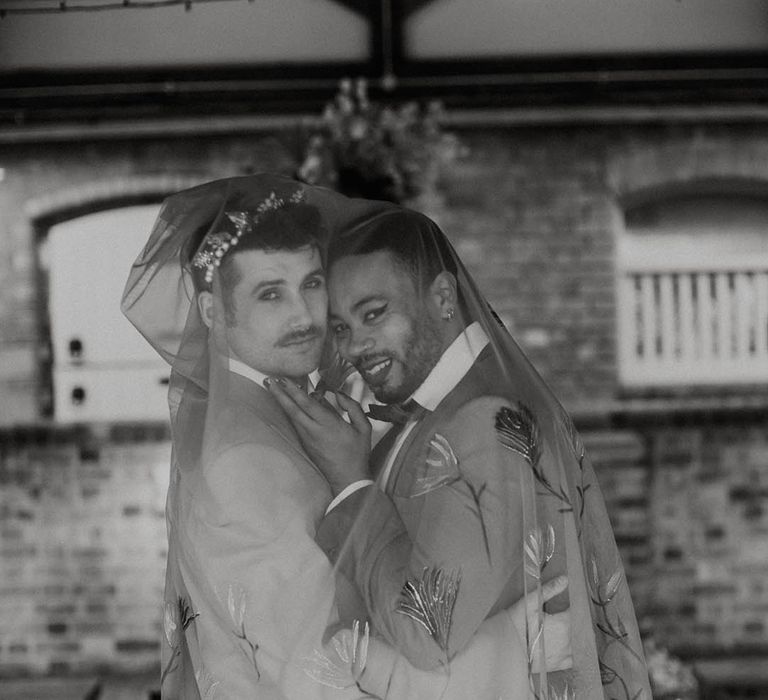 LGBTQI+ couple embracing under and embroidered veil 