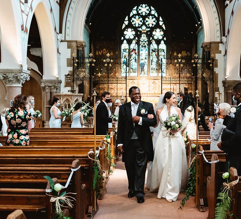 Bride and groom exit their church wedding ceremony with wedding guests wearing face masks