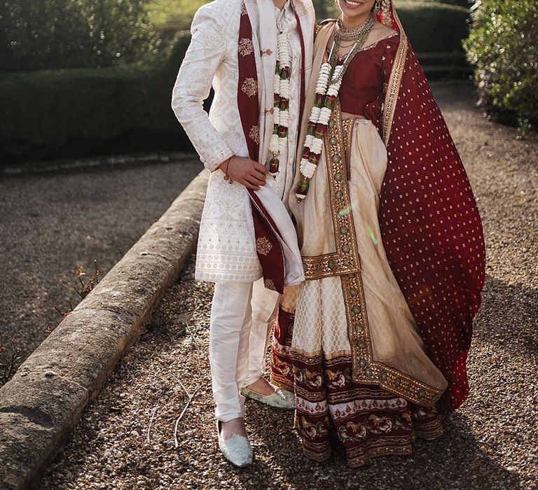 Bride and groom smile together in traditional wedding attire wearing Jaimalas