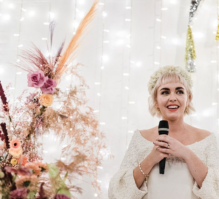 Bride wearing white flower headband and  pearl bracelet gives a bridal speech at her wedding