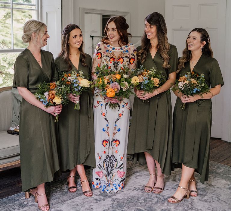 Bridesmaids in olive green wrap dresses and yellow and blue bouquets with bride in colourful wedding dress