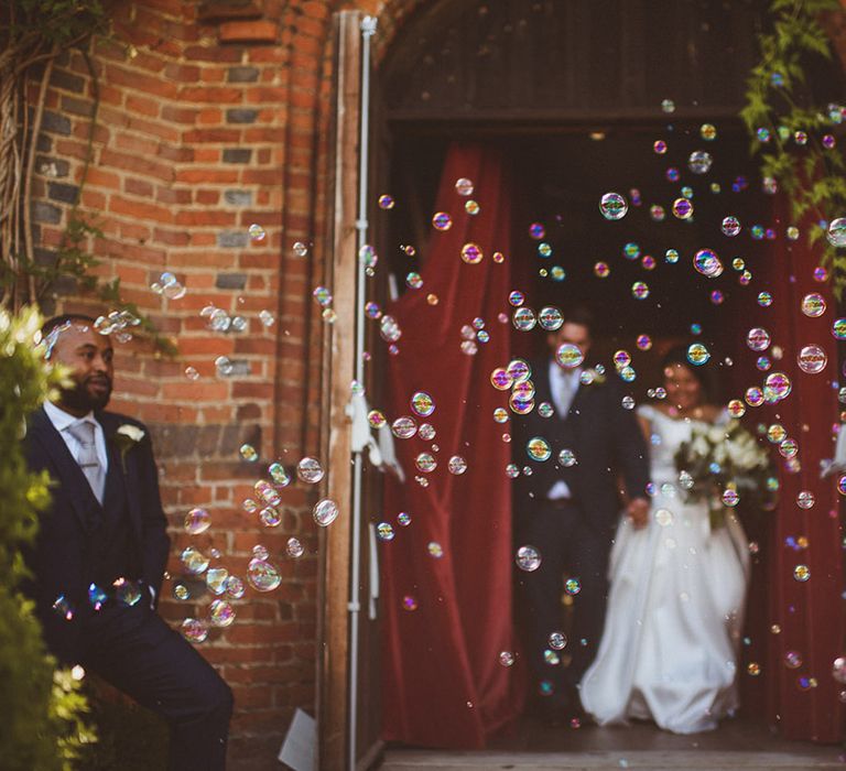 Bride and groom exit their ceremony to bubbles instead of confetti with groomsmen in blue suits