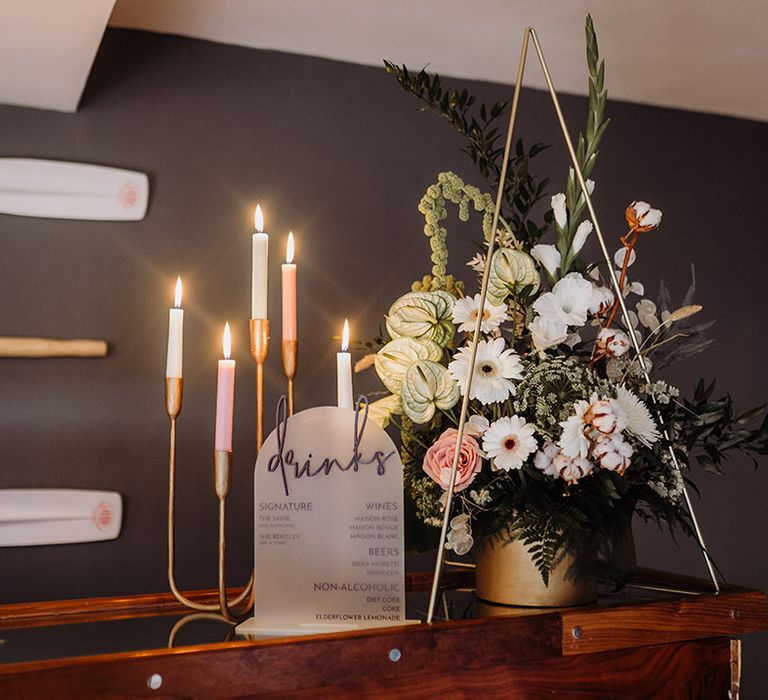 Colourful candles inna gold candle holder with a drinks menu sign and pretty florals 