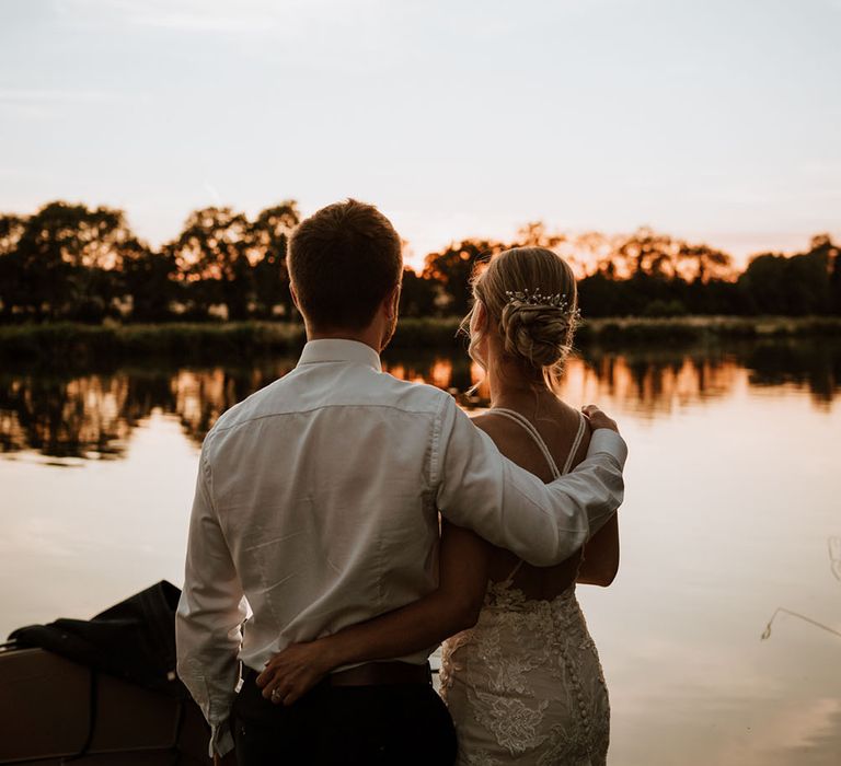 Bride & groom embrace and look across the Thames as the sun begins to set during golden hour 