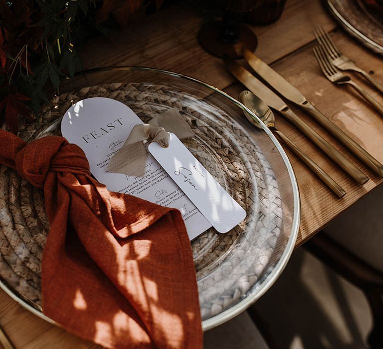 Wicker placemats with gold rimmed charger plates, orange napkins and gold cutlery for an autumnal tablescape