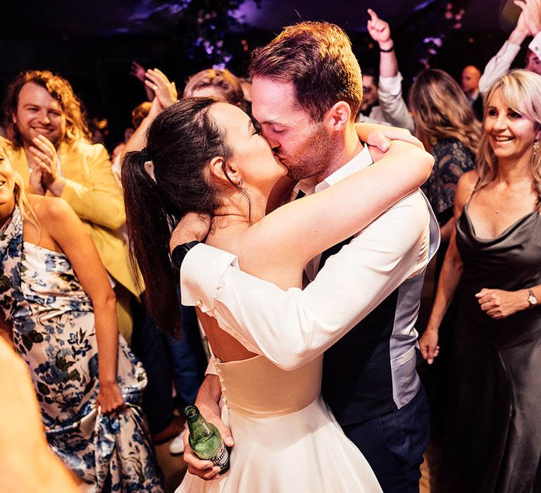 Bride and groom share a kiss on the dancefloor surrounded by their guests 