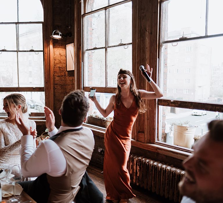 Bridesmaid in burnt orange bridesmaid dress dances during wedding reception 