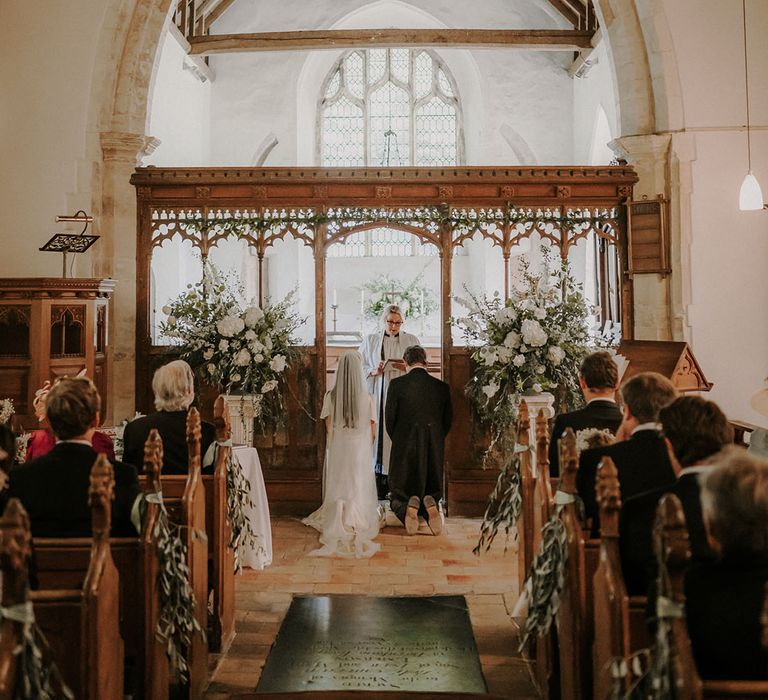 Bride and groom kneel for their traditional church wedding ceremony with white flower displays decorating the church