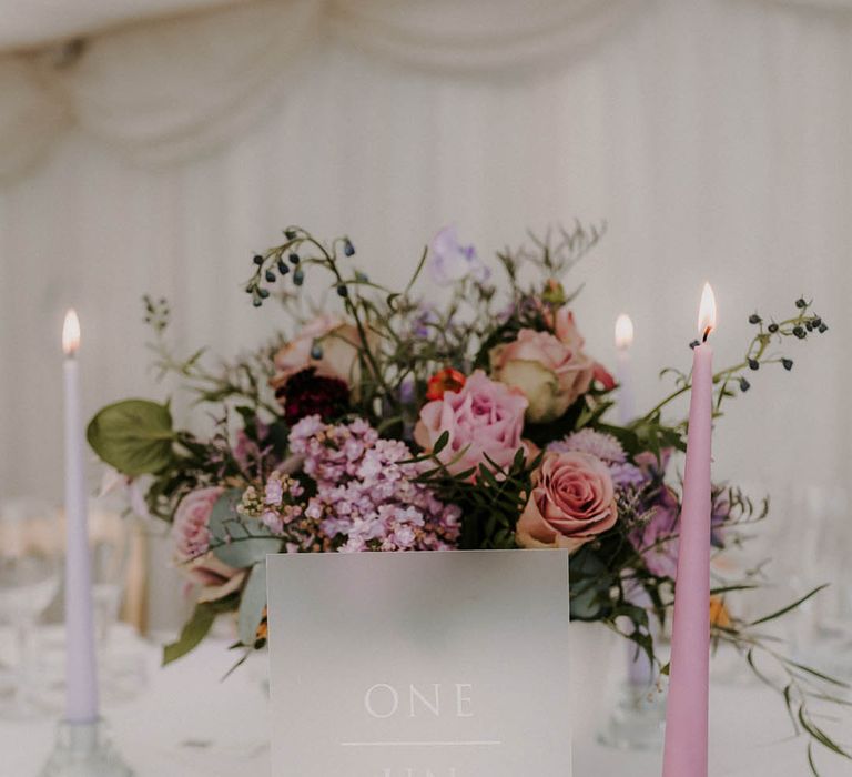 Lilac and purple wedding flowers with purple taper candles and tea lights with frosted wedding table number sign 