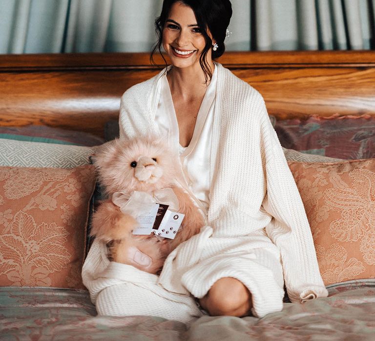 The bride sits with a pink fluffy bear present and cards in a robe before the wedding 