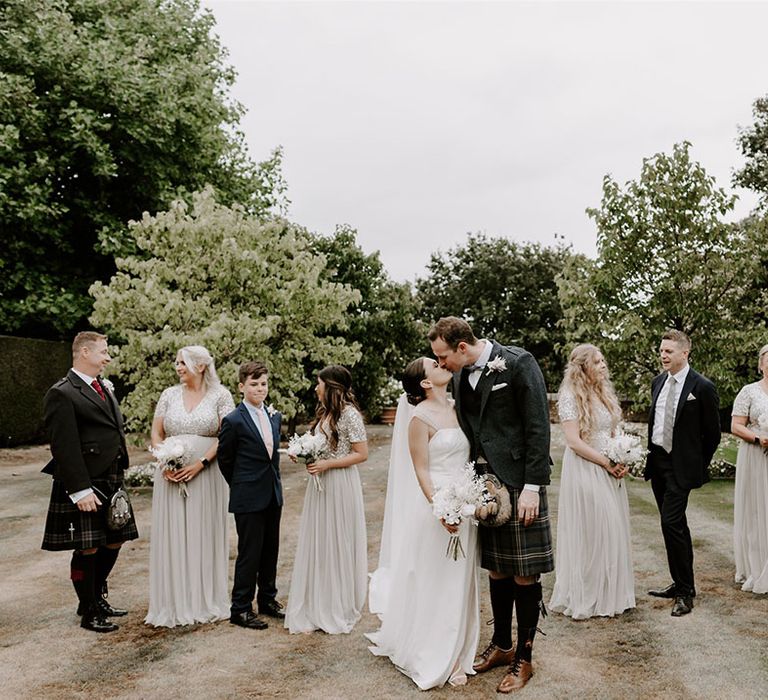 Wedding party shot of the bride and groom kissing with their bridesmaids and groomsmen 