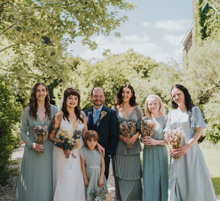 Wedding party wearing mismatched sage green and baby blue bridesmaid dresses holding dried flower bouquets