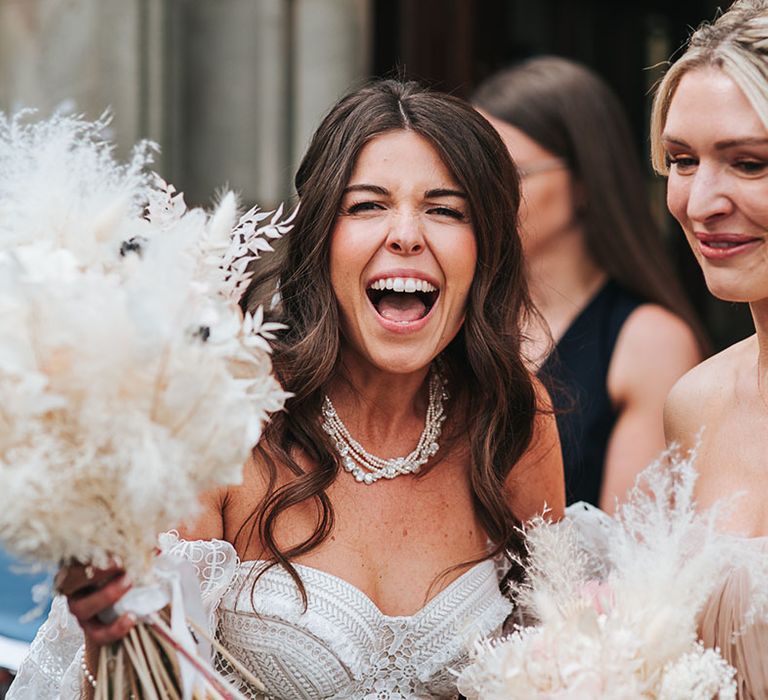 Bride with curled brown hair wearing a pearl necklace in a boho lace strapless gown and dried grass and flower bouquet 