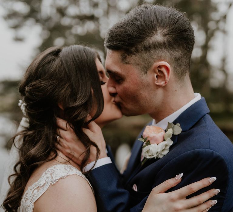 Bride in lace short sleeve wedding dress embraces her groom in blue three piece suit 