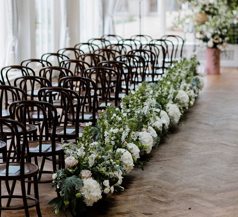 White & green floral arrangements line black chairs along the aisle