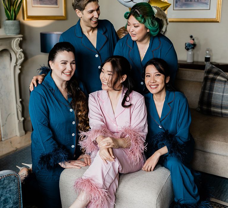 Bride wears silk pyjamas with feather detailing and sits alongside her bridal party in silk blue pyjamas 