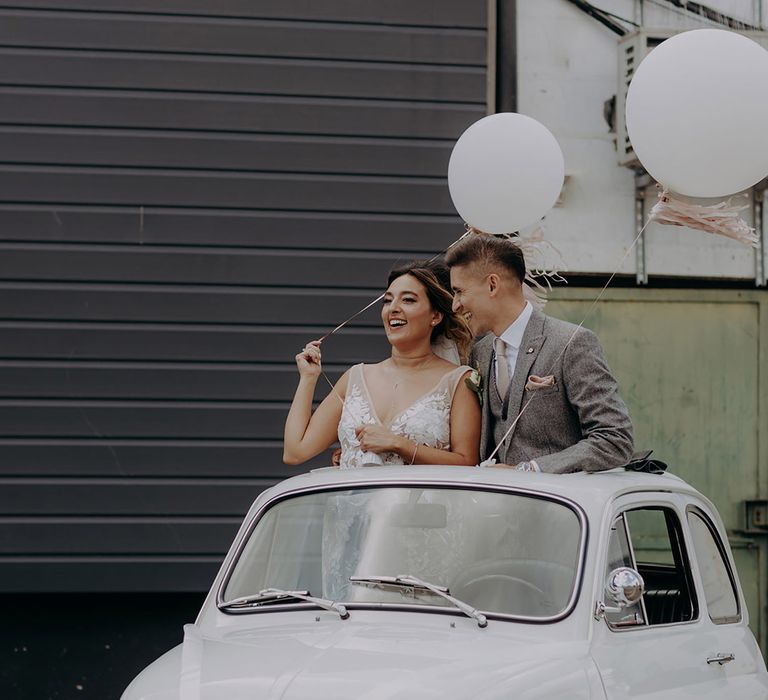 Bride and groom in a classic fiat 500 wedding car with foliage bumper decor and balloons 