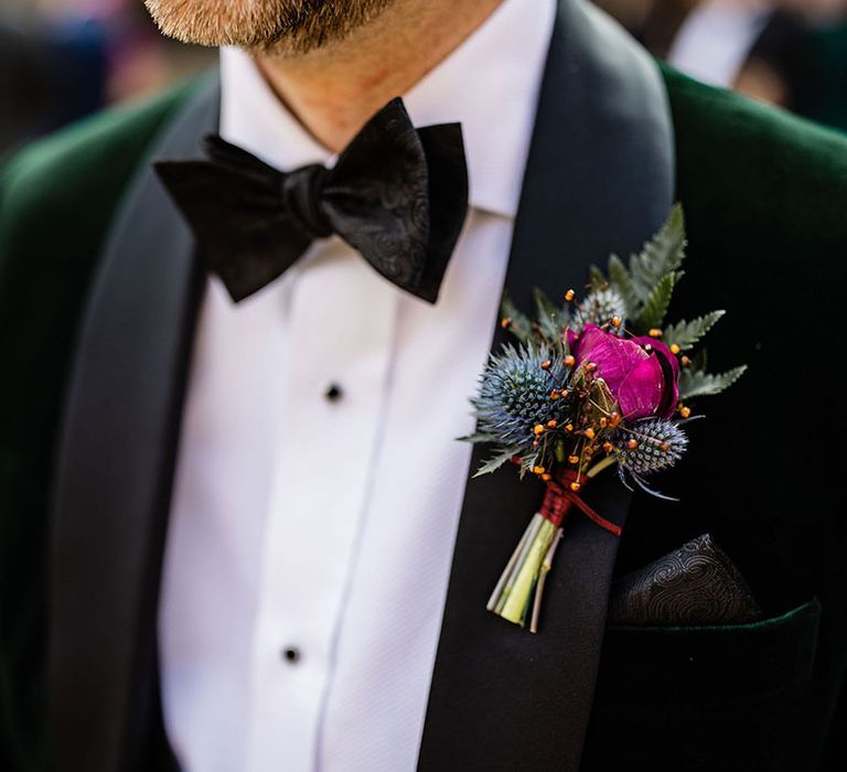 Groom wearing a fun green velvet tuxedo wearing a pink flower and thistle buttonhole 