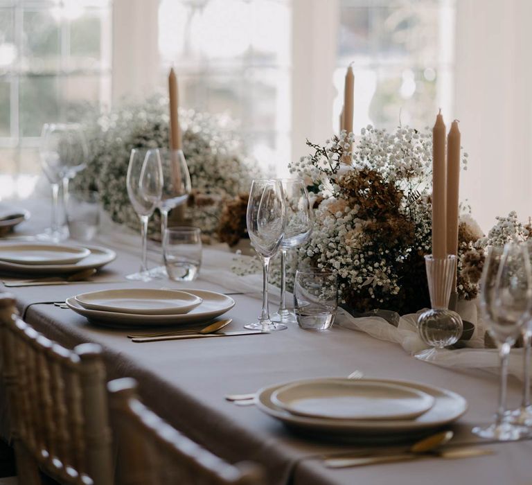 Minimalistic wedding tablescape with clean, soft neutrals, a tulle tablerunner, neutral tapered candles and large neutral coloured baby's-breath table arrangements