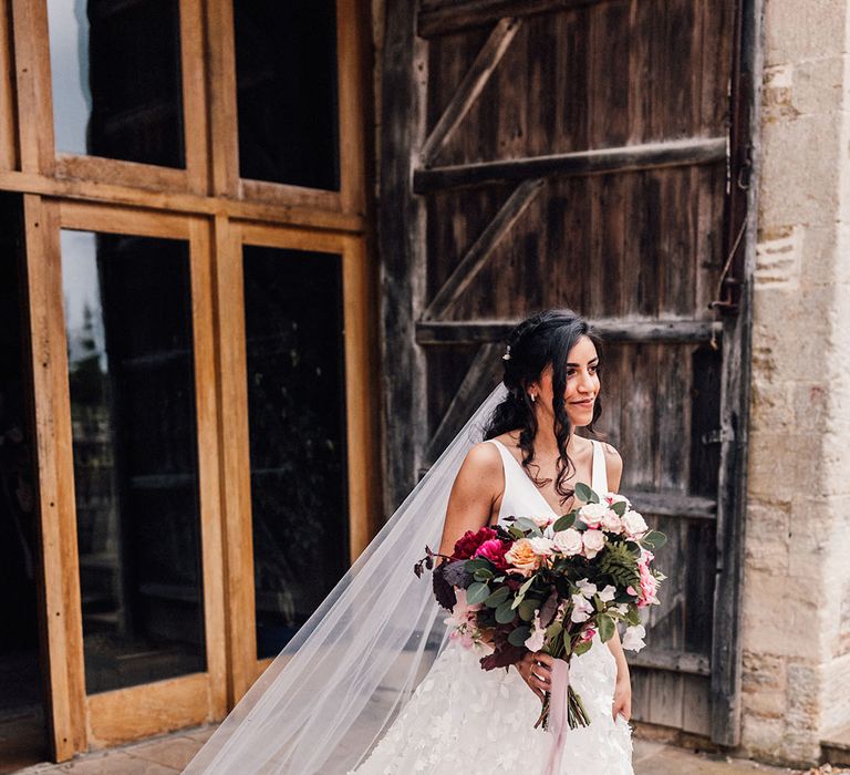 Savin London floral appliqué wedding dress with front slit worn with a cathedral length veil with embroider edge detail for barn wedding 