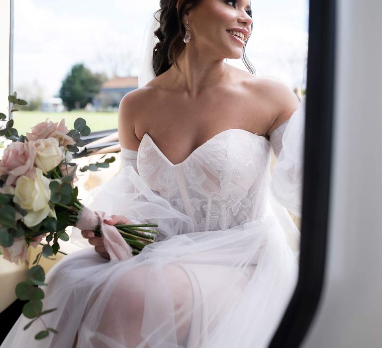 Bride in ethereal off the shoulder wedding dress with detachable puff tulle sleeves and embroidered rose 3d appliqué details holding blush garden rose and eucalyptus bridal bouquet 