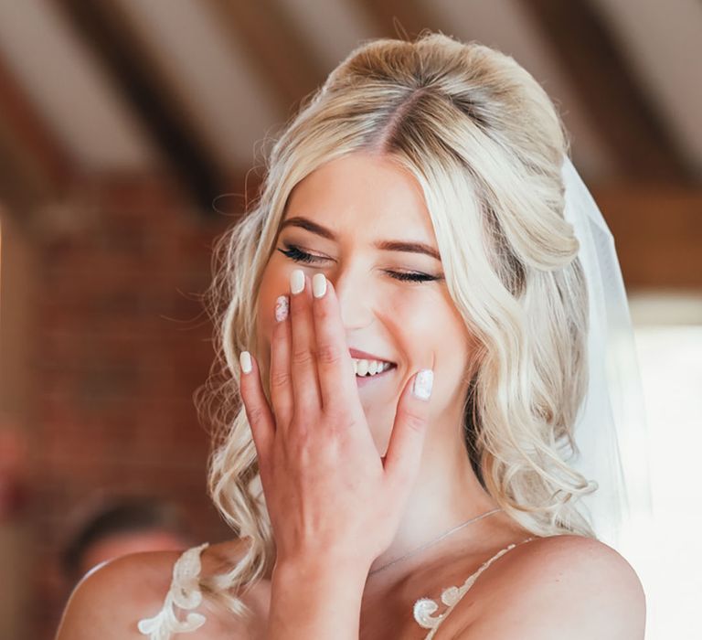 Laughing bride with white wedding nails with pink flower nail art wearing a lace wedding dress and veil 