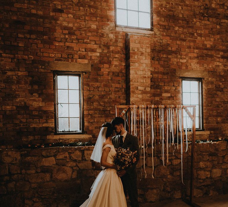 Exmouth Country Lodge wedding inspiration in Devon with DIY ribbon altar decoration with the bride and groom sharing an intimate moment 