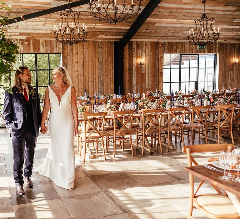 Bride in fitted wedding dress with the groom in a three piece blue suit walking around the wedding reception decorated with blue and orange decor 