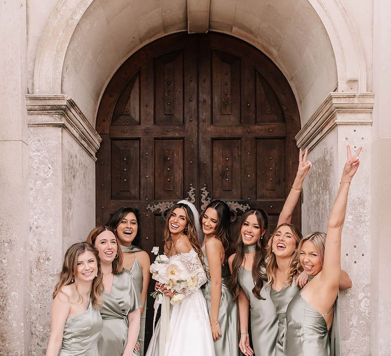 Bridal party in satin green mismatched bridesmaid dresses with the bride for fun group wedding photo 