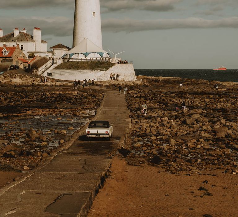 Bride riding in the wedding car to the lighthouse wedding venue for retro coastal wedding 