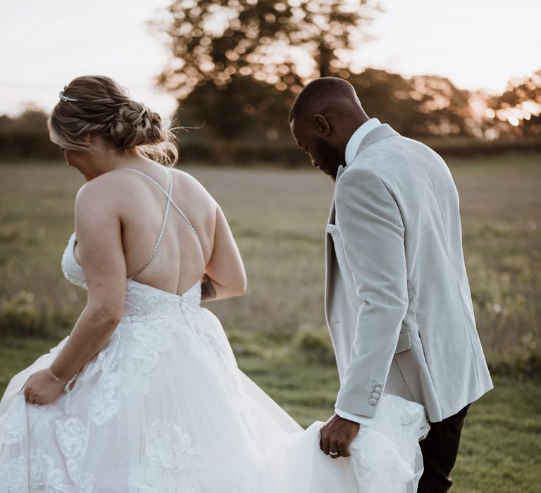 Bride in floral lace wedding dress with beaded straps walking around the venue with the groom in a velvet grey suit jacket 