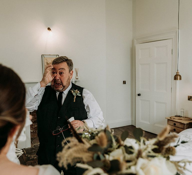 Father of the bride gets emotional and wipes his tears as he sees the bride for the first time in her wedding dress 