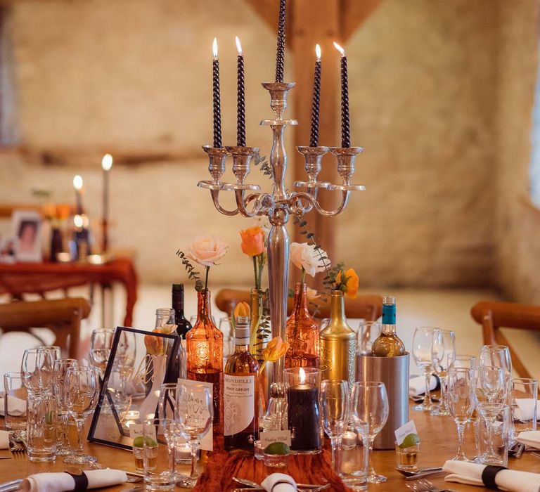 Golden candelabras with black polka dot tapered candles on rust orange wedding tablescape at Kingscote Barn Tetbury wedding venue with fairy lights and festoon lighting 