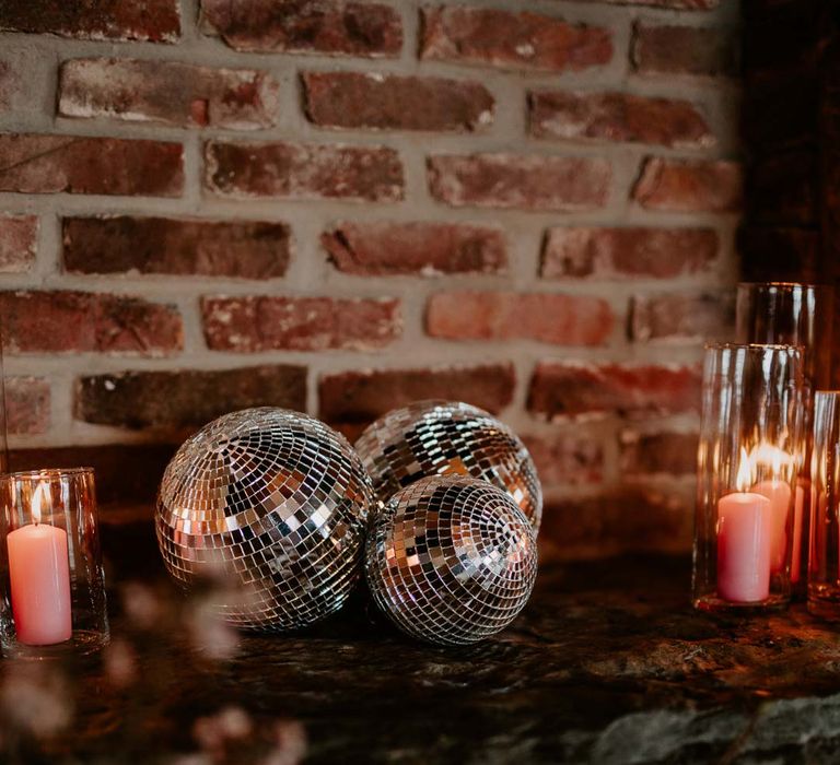 Disco ball wedding decorations with pink tapered candles in tall glass candle jars on top of exposed brick fireplace at Willow Marsh Farm Loughborough 