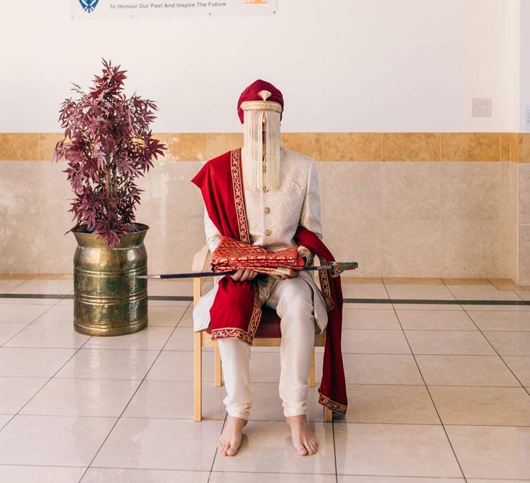 Groom in traditional white and gold sherwani sitting on chair at Indian-English fusion wedding 